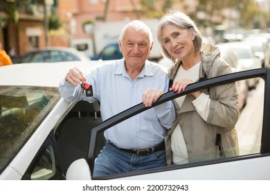 A senior couple standing beside their car
